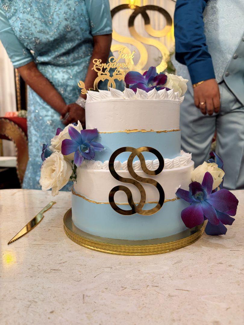 Two-tier white and blue engagement cake with a gold monogram and orchids
